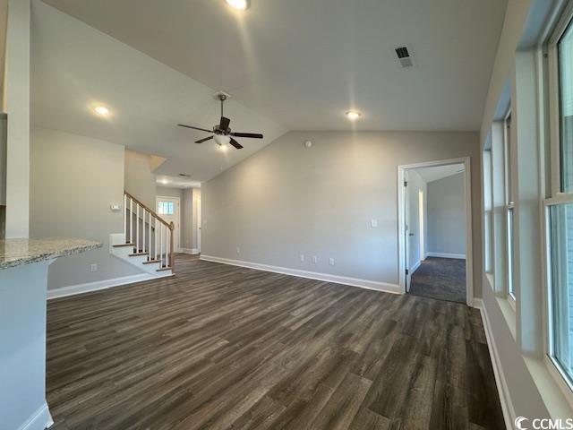 unfurnished living room with ceiling fan, dark wood-type flooring, baseboards, vaulted ceiling, and stairs