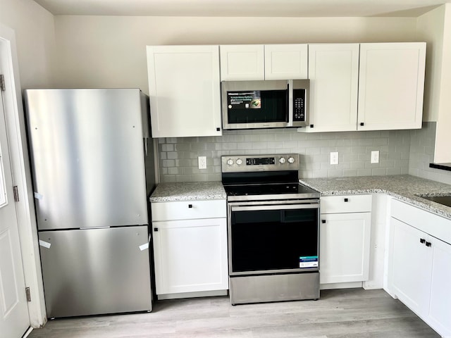 kitchen featuring white cabinets, backsplash, light stone countertops, stainless steel appliances, and light wood-type flooring