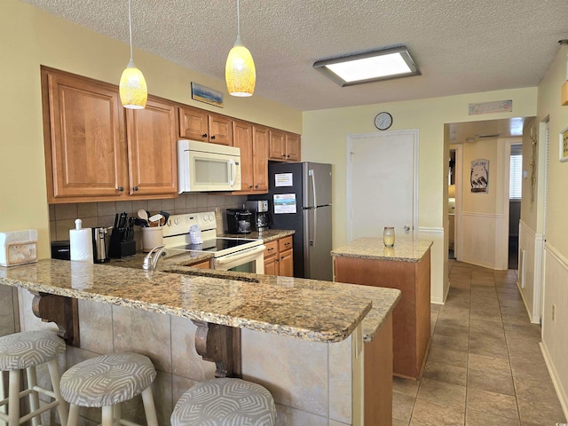 kitchen with backsplash, white appliances, light stone counters, kitchen peninsula, and pendant lighting