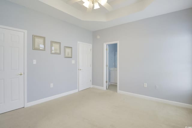 unfurnished bedroom with light colored carpet, connected bathroom, a tray ceiling, and ceiling fan