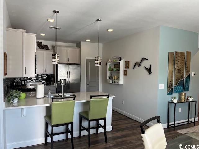 kitchen featuring a breakfast bar area, hanging light fixtures, stainless steel fridge with ice dispenser, a peninsula, and dark wood-style floors