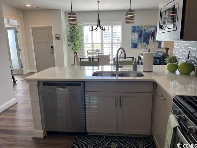 kitchen with a sink, stainless steel appliances, dark wood-type flooring, light countertops, and a chandelier