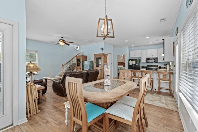 dining room with visible vents, light wood-style flooring, ceiling fan with notable chandelier, recessed lighting, and stairs