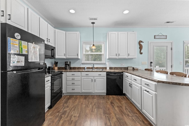 kitchen with dark countertops, a peninsula, black appliances, and a sink