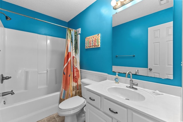 full bathroom featuring shower / tub combo with curtain, toilet, a textured ceiling, wainscoting, and vanity