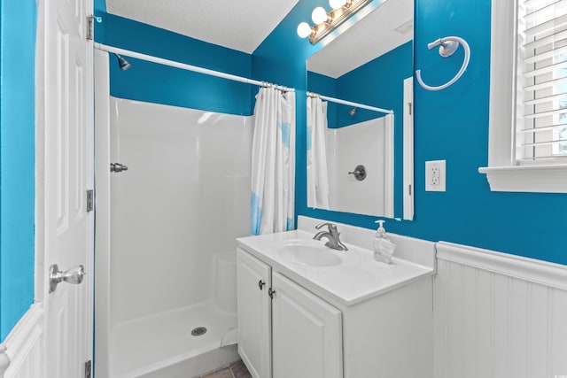 bathroom with a wainscoted wall, a stall shower, vanity, and a textured ceiling