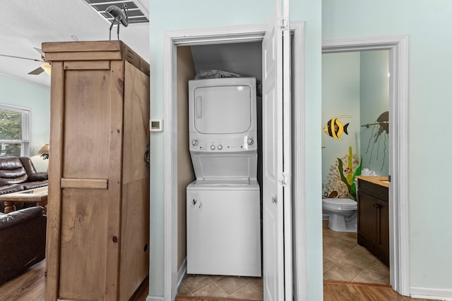 laundry room featuring tile patterned floors, stacked washer / drying machine, a ceiling fan, and laundry area