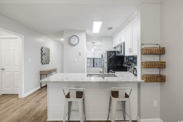 kitchen featuring stainless steel appliances, light hardwood / wood-style floors, white cabinetry, kitchen peninsula, and a breakfast bar area