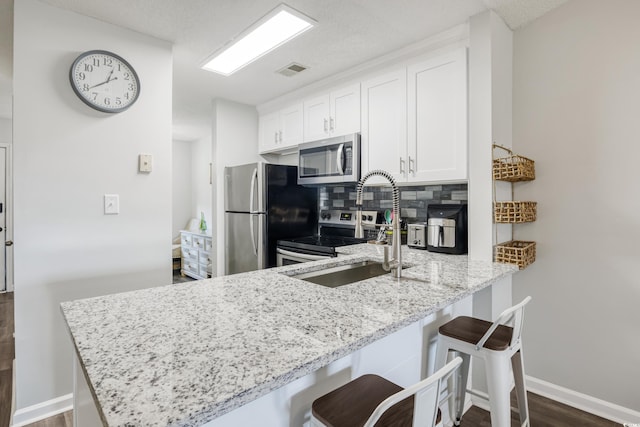 kitchen featuring a kitchen breakfast bar, dark hardwood / wood-style floors, appliances with stainless steel finishes, kitchen peninsula, and white cabinets