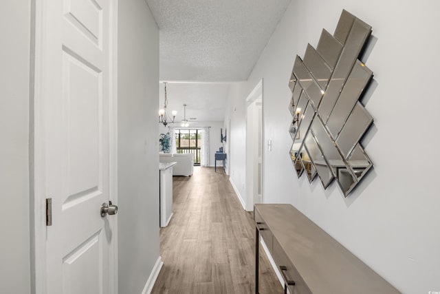 corridor featuring a textured ceiling, hardwood / wood-style flooring, and a chandelier