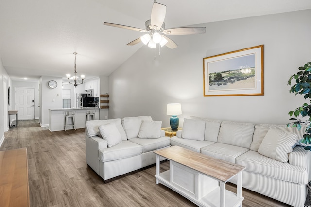 living room featuring ceiling fan with notable chandelier, vaulted ceiling, and wood-type flooring