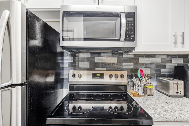 kitchen featuring white cabinetry, backsplash, stainless steel appliances, and light stone countertops