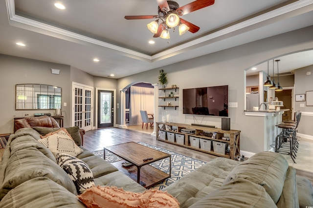 living room featuring ceiling fan, ornamental molding, a tray ceiling, and light hardwood / wood-style floors