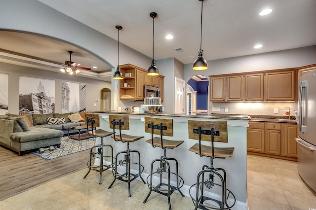 kitchen with ceiling fan, hanging light fixtures, stainless steel appliances, a breakfast bar, and light wood-type flooring