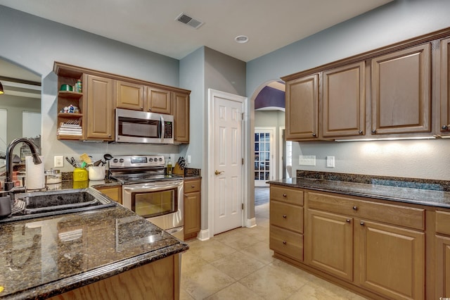 kitchen with stainless steel appliances, dark stone countertops, light tile patterned flooring, and sink