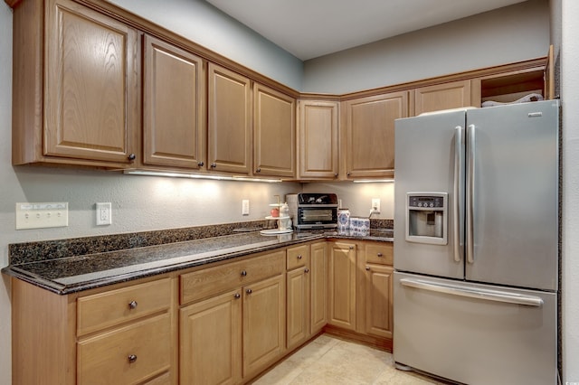 kitchen featuring dark stone counters, light tile patterned flooring, and stainless steel fridge with ice dispenser