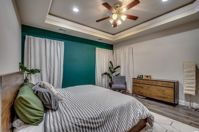 bedroom with light hardwood / wood-style flooring, a tray ceiling, ceiling fan, and crown molding