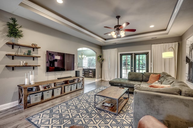 living room with ceiling fan with notable chandelier, a tray ceiling, hardwood / wood-style flooring, and crown molding