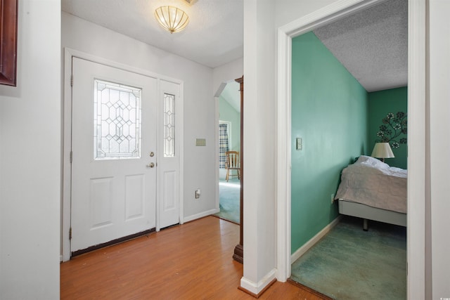 foyer featuring light wood-style floors, arched walkways, a textured ceiling, and baseboards