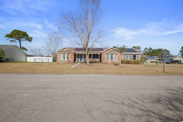 single story home with a front yard, fence, solar panels, and brick siding