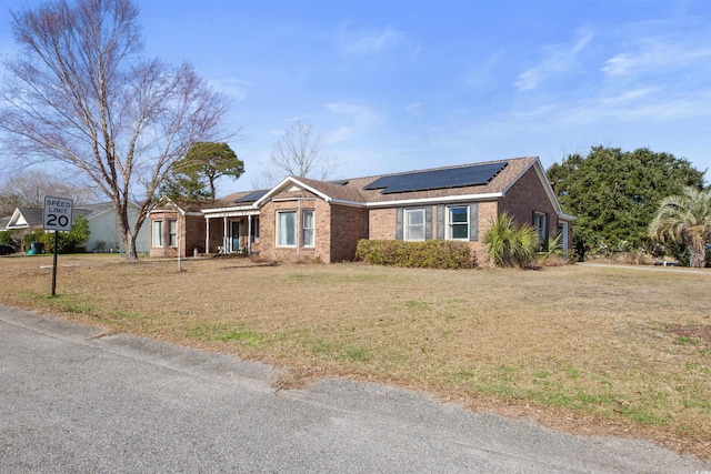 ranch-style home with a front lawn, brick siding, and roof mounted solar panels