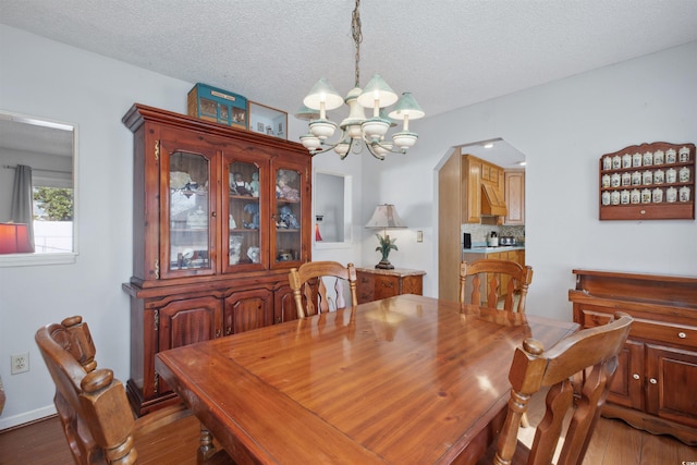 dining area with arched walkways, a textured ceiling, wood finished floors, a chandelier, and baseboards