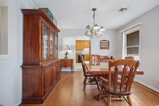 dining room with a chandelier, light wood-style flooring, a textured ceiling, and visible vents