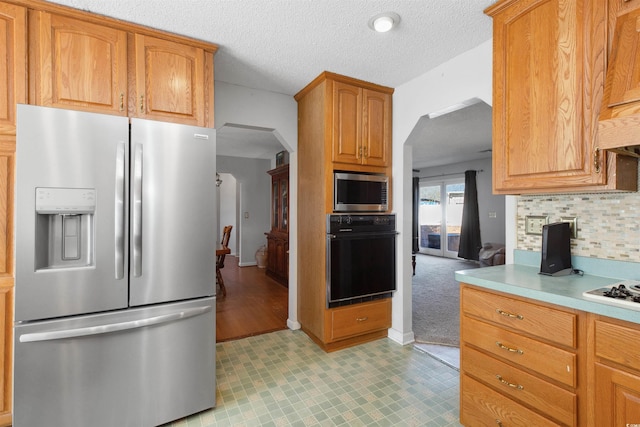 kitchen with tasteful backsplash, arched walkways, stainless steel appliances, a textured ceiling, and light countertops