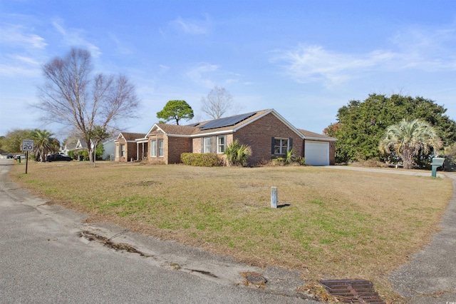 ranch-style house with a garage, roof mounted solar panels, brick siding, and a front lawn