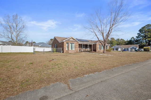 ranch-style house with a front yard, fence, solar panels, and brick siding