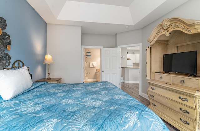 bedroom with a tray ceiling, hardwood / wood-style floors, and ensuite bathroom