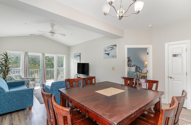 dining space with ceiling fan with notable chandelier, light hardwood / wood-style floors, and vaulted ceiling