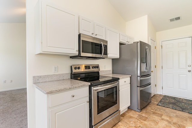 kitchen with white cabinetry, light stone counters, stainless steel appliances, lofted ceiling, and light colored carpet