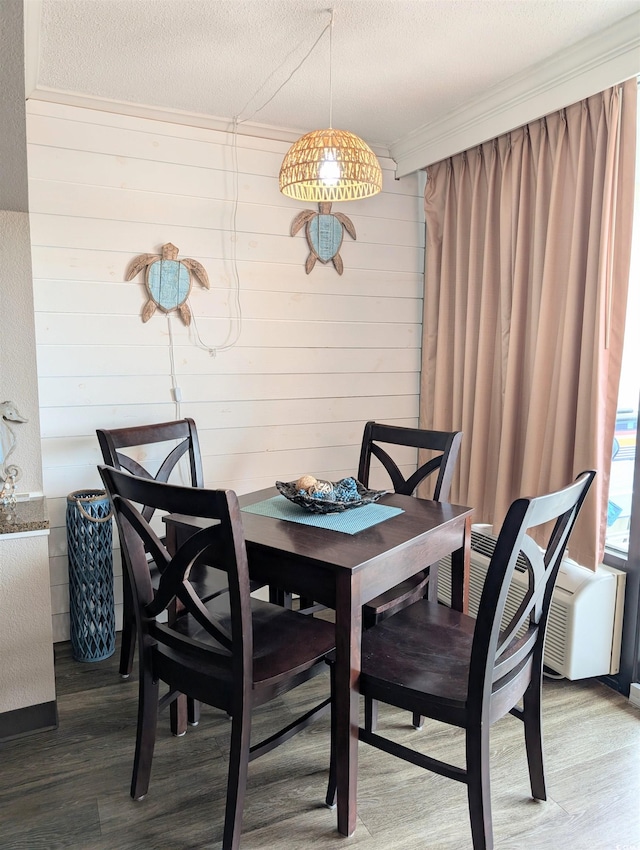 dining space with wooden walls, a textured ceiling, and hardwood / wood-style floors