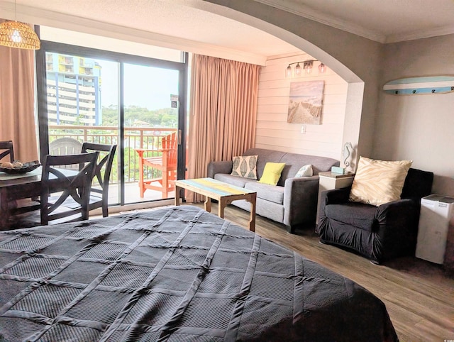 bedroom featuring access to exterior, a textured ceiling, crown molding, hardwood / wood-style flooring, and wooden walls