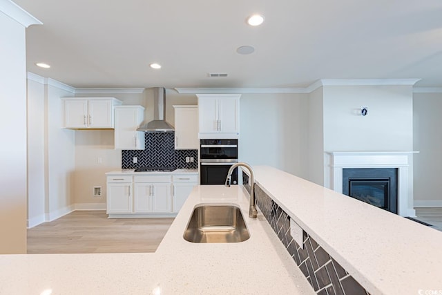 kitchen with white cabinets, double oven, wall chimney exhaust hood, and sink