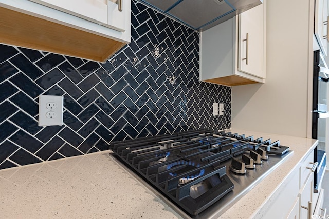 kitchen featuring decorative backsplash, light stone counters, wall chimney exhaust hood, gas stovetop, and white cabinets