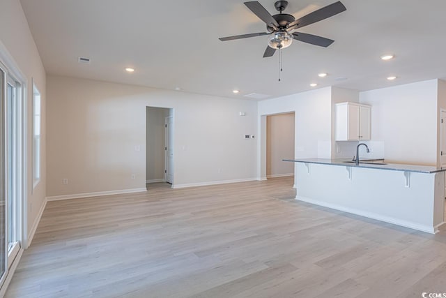 unfurnished living room with ceiling fan, sink, and light wood-type flooring