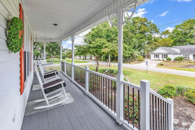 wooden terrace featuring a lawn and covered porch