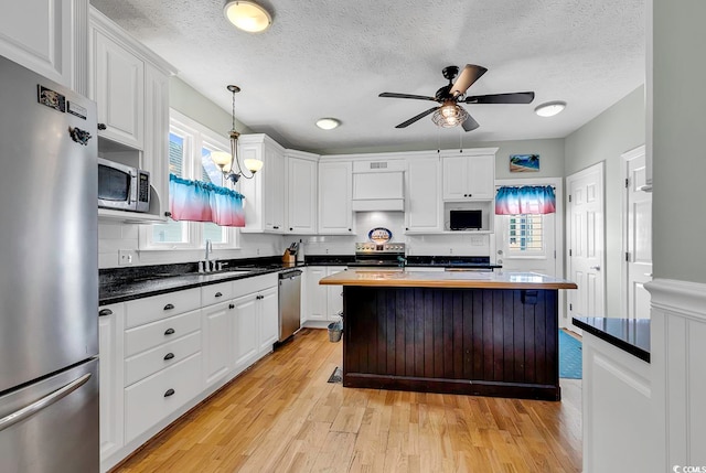 kitchen featuring light wood-type flooring, wood counters, ceiling fan with notable chandelier, white cabinetry, and appliances with stainless steel finishes