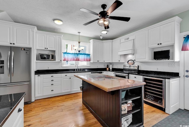 kitchen with wine cooler, light wood-type flooring, stainless steel appliances, a center island, and ceiling fan with notable chandelier