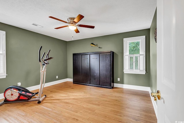 workout area featuring ceiling fan, a textured ceiling, and light wood-type flooring