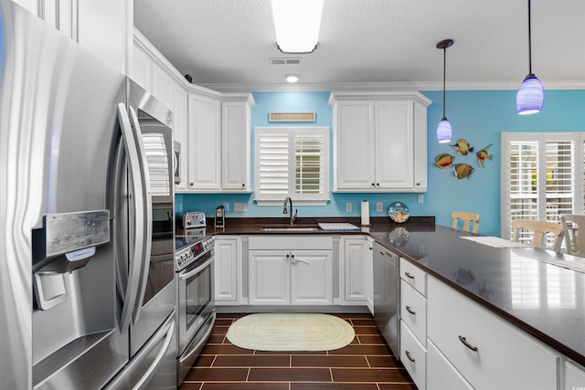 117B Ocean Blvd S, Surfside Beach, SC 29575 - kitchen with white cabinets, stainless steel appliances, dark countertops, a sink, and hanging light fixtures
