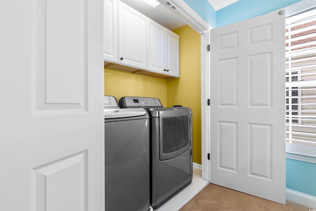 clothes washing area featuring a wealth of natural light, light carpet, washer and dryer, and cabinets