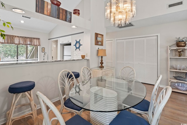 dining space featuring a notable chandelier, high vaulted ceiling, and light hardwood / wood-style flooring