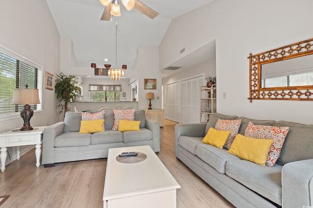 living room with ceiling fan with notable chandelier, light hardwood / wood-style floors, and high vaulted ceiling