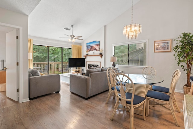 dining area featuring a textured ceiling, ceiling fan with notable chandelier, hardwood / wood-style flooring, and high vaulted ceiling