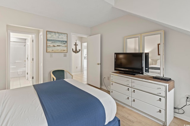 bedroom featuring light wood-type flooring, ensuite bathroom, and vaulted ceiling