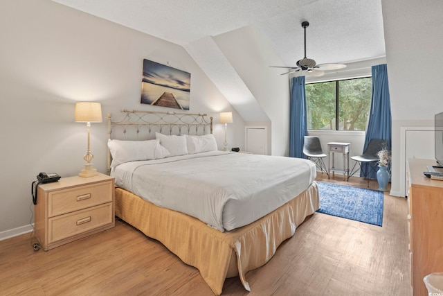 bedroom with a textured ceiling, ceiling fan, light hardwood / wood-style floors, and lofted ceiling