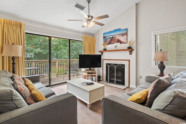 living room with vaulted ceiling, hardwood / wood-style flooring, ceiling fan, a textured ceiling, and a tiled fireplace